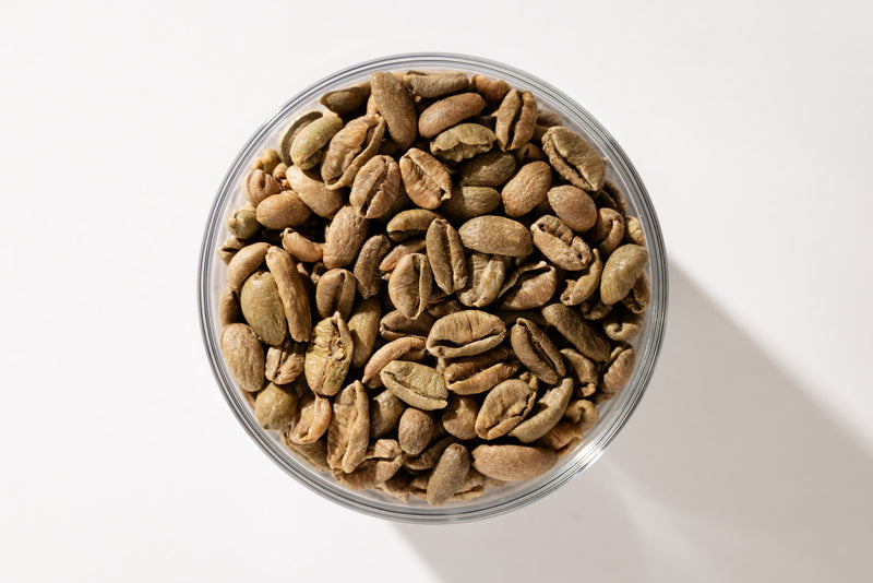 A glass bowl of roasted coffee beans on a plain white ground. A sample, set aside.