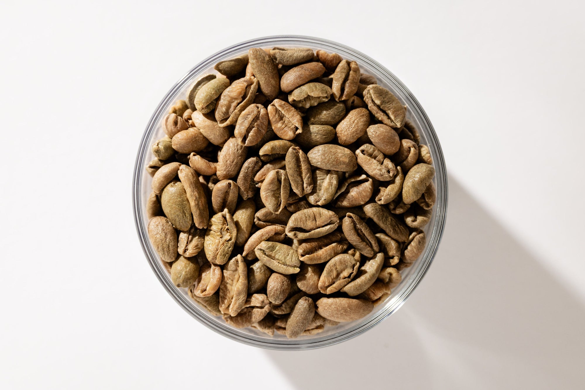 A glass bowl of roasted coffee beans on a plain white ground. A sample, set aside.