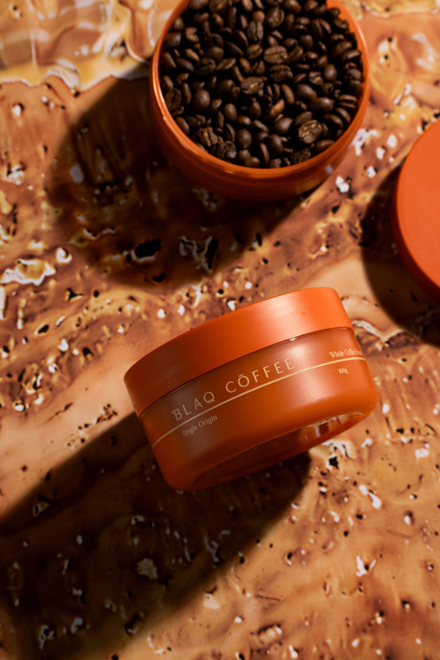 A Blaq Coffee jar and a bowl of roasted beans on a raw, marbled clay-toned surface.