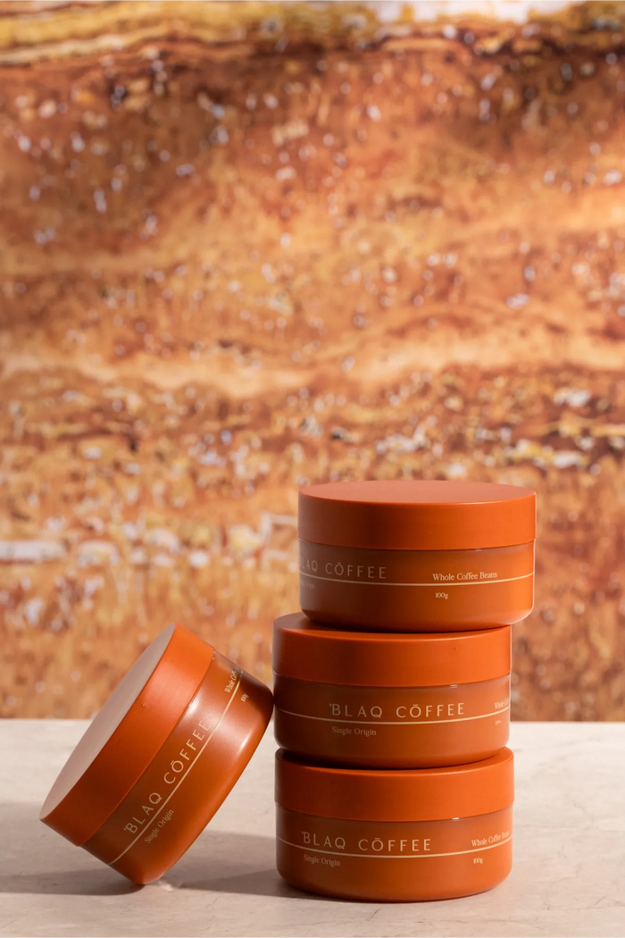 Blaq Coffee Colombia Trio. Three tins stacked on travertine in warm light.
