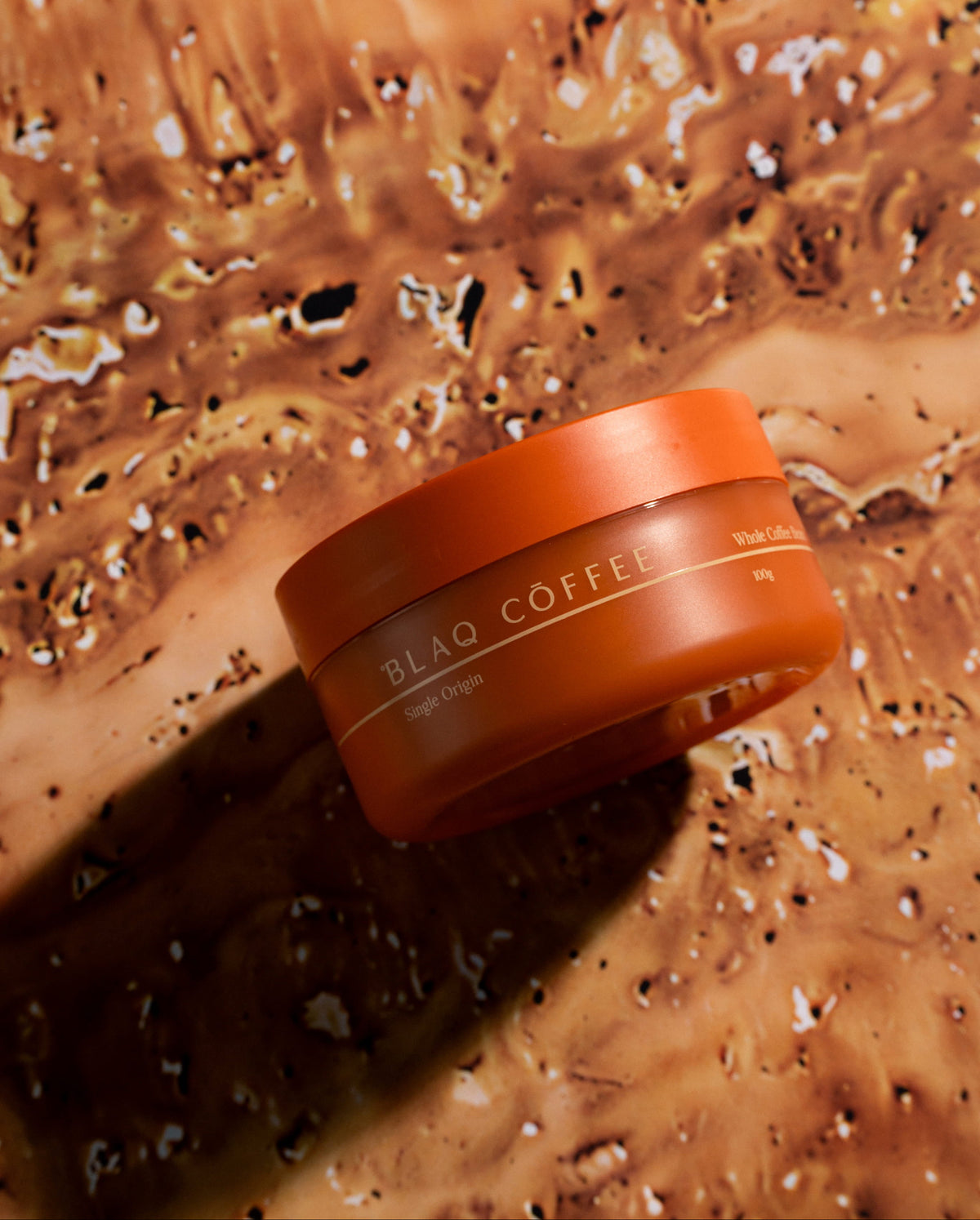 An orange Blaq Coffee container on a textured ground.